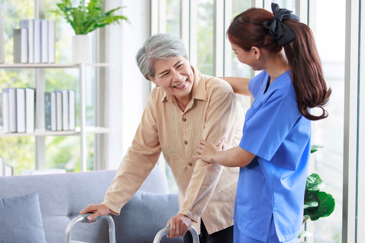 Nurse in blue scrubs helps smiling older patient with walker