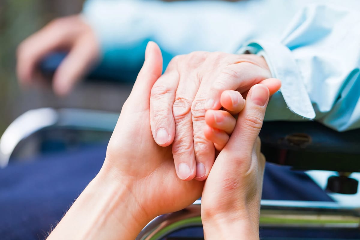 Caring hands gently hold an elderly person's hand in a wheelchair,